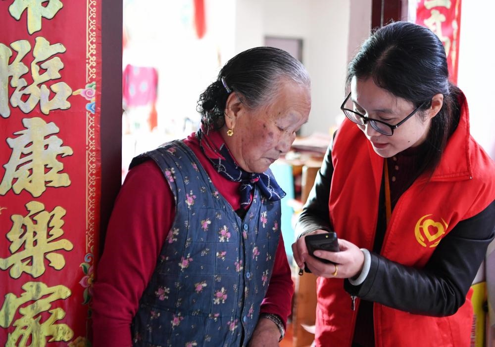 在福州市長樂區(qū)航城街道籌岐村，智慧養(yǎng)老平臺派駐社區(qū)的助老員（右）在為老人陳鳳英（左）講解養(yǎng)老定制手機(jī)的用法（2021年11月26日攝）。新華社記者 魏培全 攝