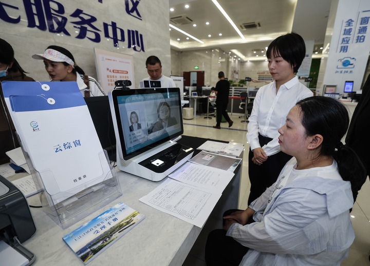 在浙江省嘉興市秀洲區(qū)王江涇鎮(zhèn)便民服務(wù)中心的“跨域通辦·云綜窗”窗口，辦理開(kāi)業(yè)登記的個(gè)體工商戶(hù)（右一）通過(guò)該系統(tǒng)與江蘇省蘇州市吳江區(qū)盛澤鎮(zhèn)行政審批局工作人員視頻連線(xiàn)，進(jìn)行身份讀取及材料線(xiàn)上審核（2024年5月9日攝）。新華社記者 徐昱 攝